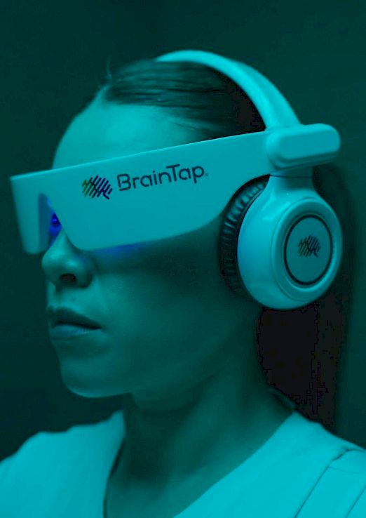 A person wearing a BrainTap headband and large turquoise headphones, with a calm face in a teal-lit setting.