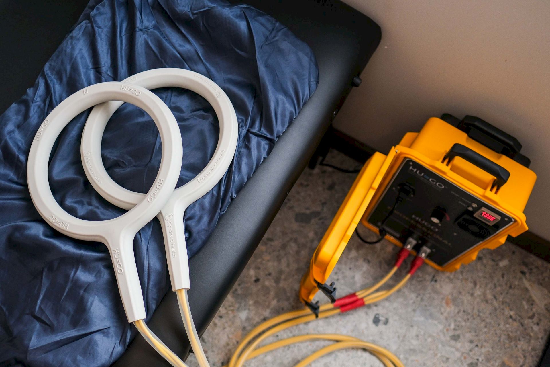 Blue fabric with a white HU-GO cable loop and an orange electronic equipment unit with wires attached nearby in the room.