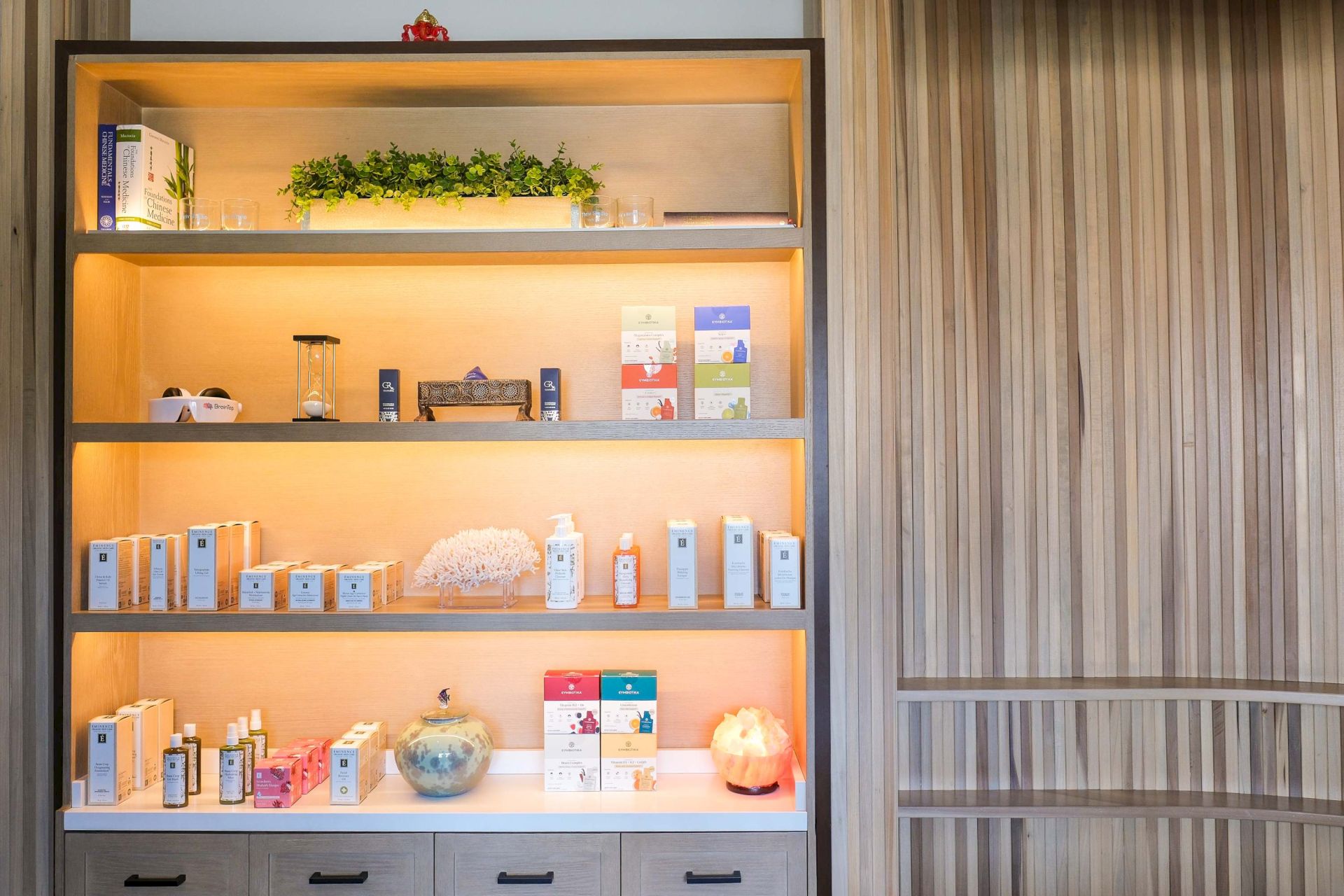 A spa display shelf stocked with skincare boxes and bottles, plus decorative plants and hourglass-like decor in warm lighting.