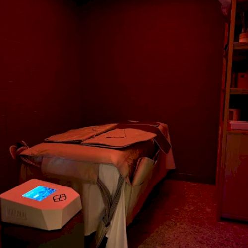 A dimly lit room with a single bed, a turntable-like device on a nearby table, and a tall cabinet; the bed is neatly made with a blanket.