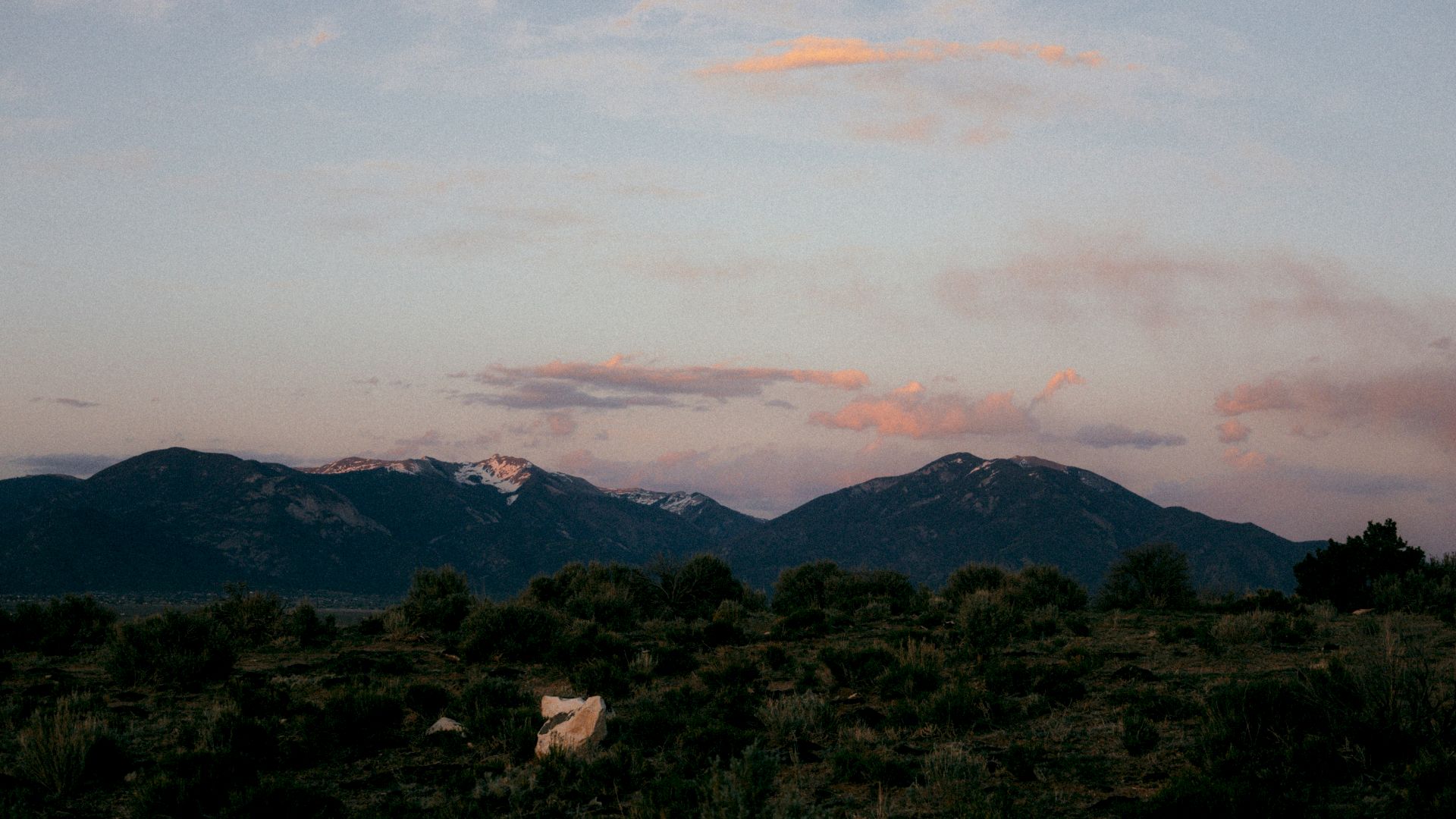 A tranquil mountain range at sunset, dark ridges under a sky of soft pastel clouds.