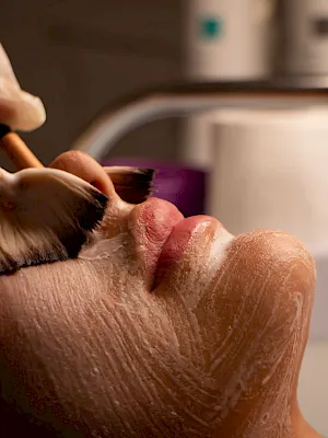 A person is shaving a man’s face with a razor and shaving cream, close-up for grooming and beard trimming.