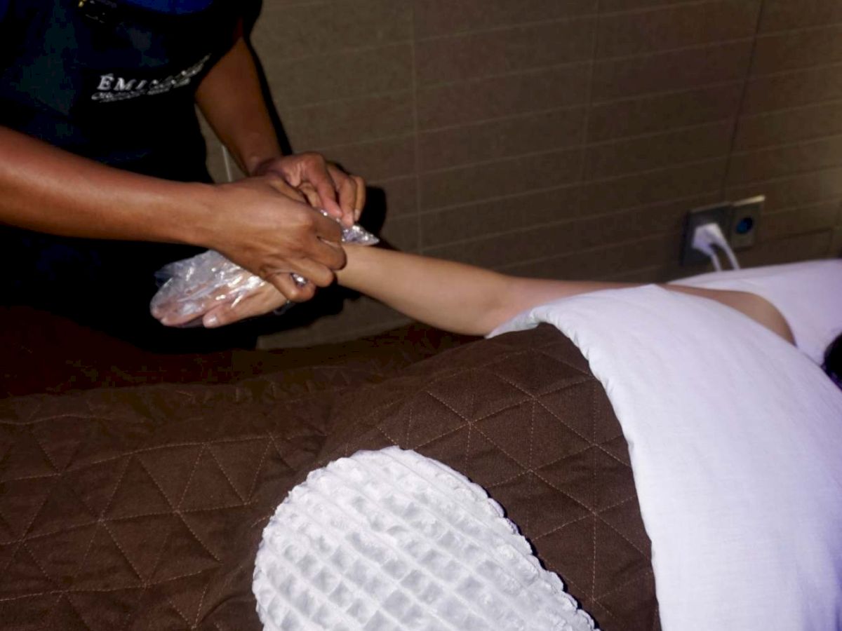 A healthcare worker in blue scrubs and a face mask is treating someone&rsquo;s leg on a bed with gloved hands.