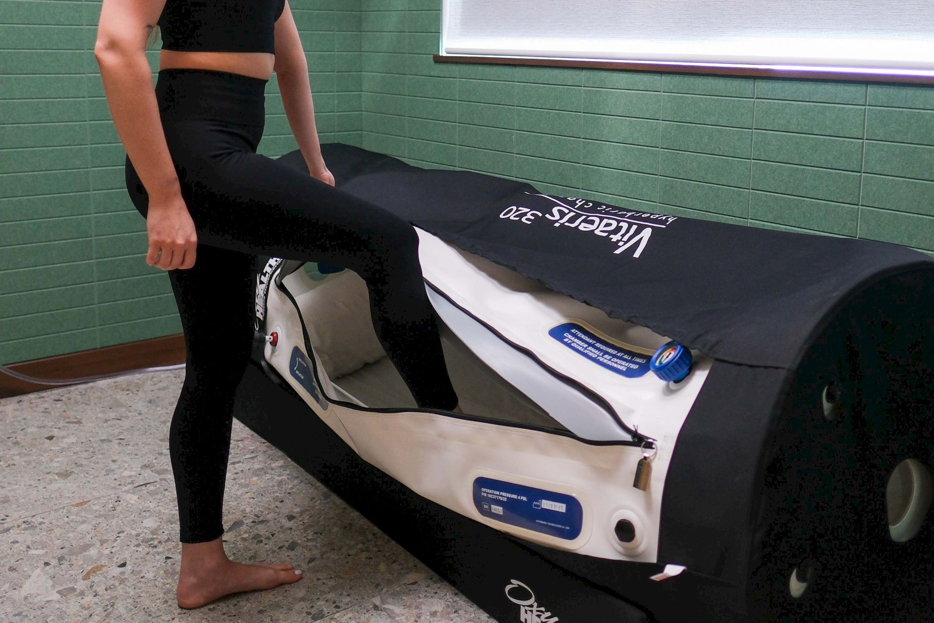 A person stretches while lying beside an inflatable recovery mat in a gym room.