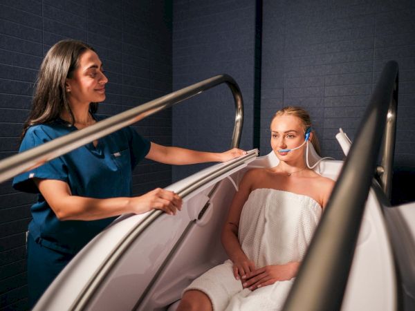 A spa attendant helps a client in a treatment chair while she wears a head headset, ready for a relaxing therapy session.